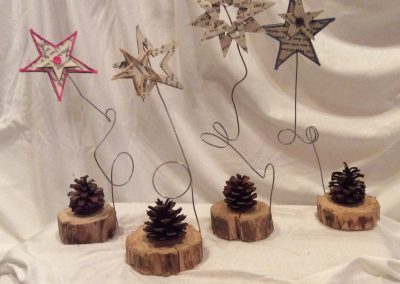 Quatres petits montage de bois avec des pommes de pins et des étoiles en papiers