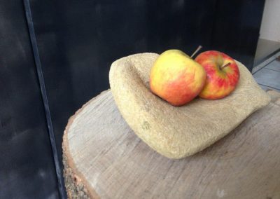 Une pierre taillée en bol avec deux pommes sur un tronçon de bois