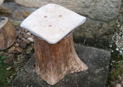 Tabouret fait d'une souche de bois avec pour assise une pierre jaune de forme carré